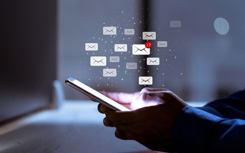 person holding a phone in the dark with the screen on and graphics of email envelopes overlaid